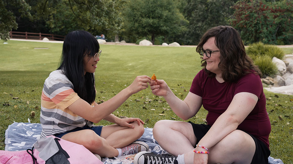 Two people eating dried mango on a picnic blanket